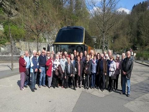 Eine große Reisegruppe steht in mehreren Reihen vor einem Reisebus, dahinter bewaldete Felsen.
