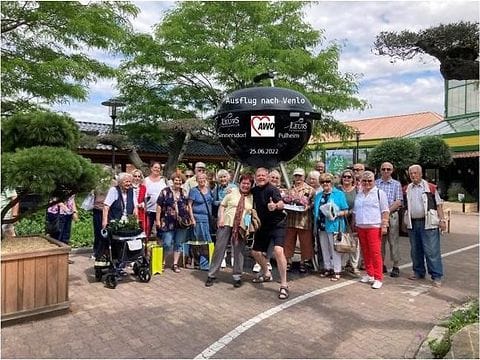Gruppenfoto von etwa dreißig Menschen auf einem Platz, in der Mitte ein Schild „Ausflug nach Venlo, 25.06.2022“ mit den Namen Sinnersdorf und Pulheim.